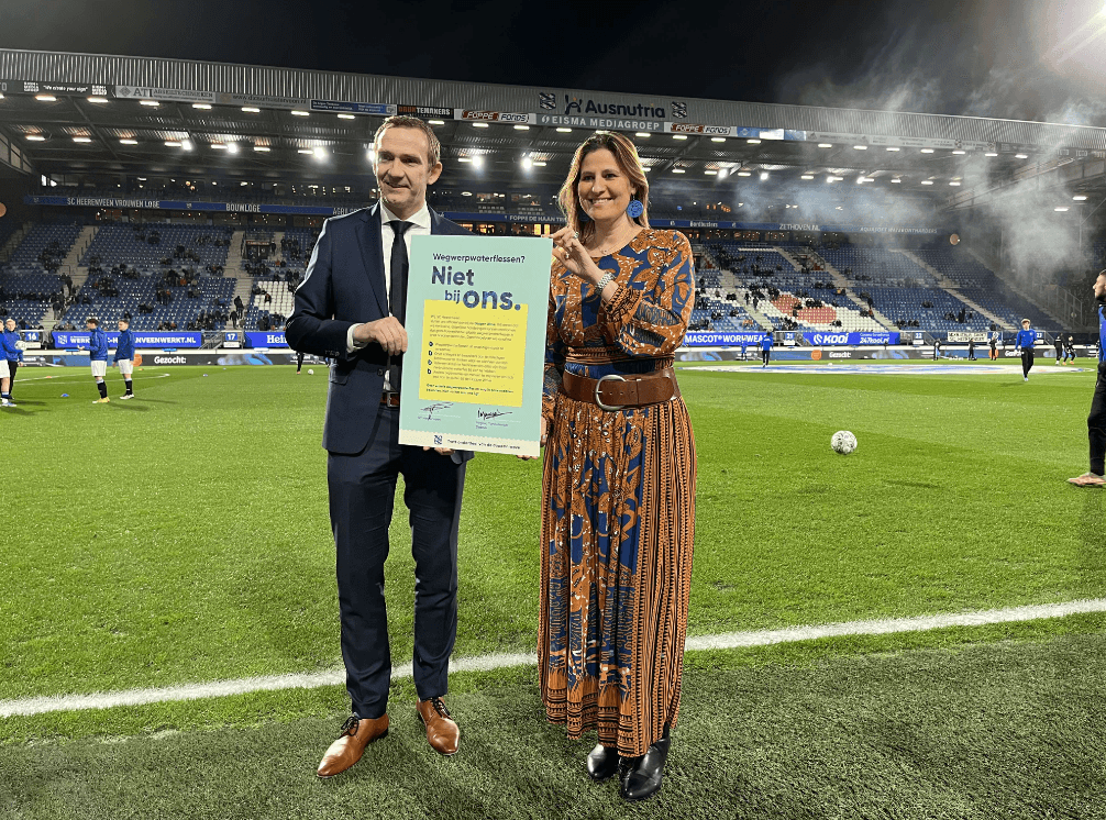 Man and woman holding a Dopper Wave pledge on the football field of sc Heerenveen