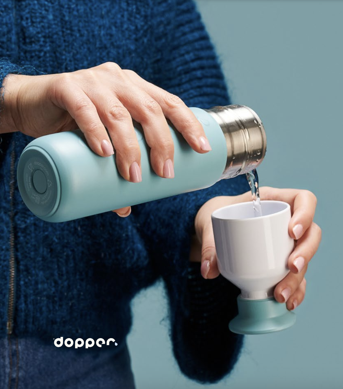 Person filling the Dopper Cup with water from the light blue bottle body