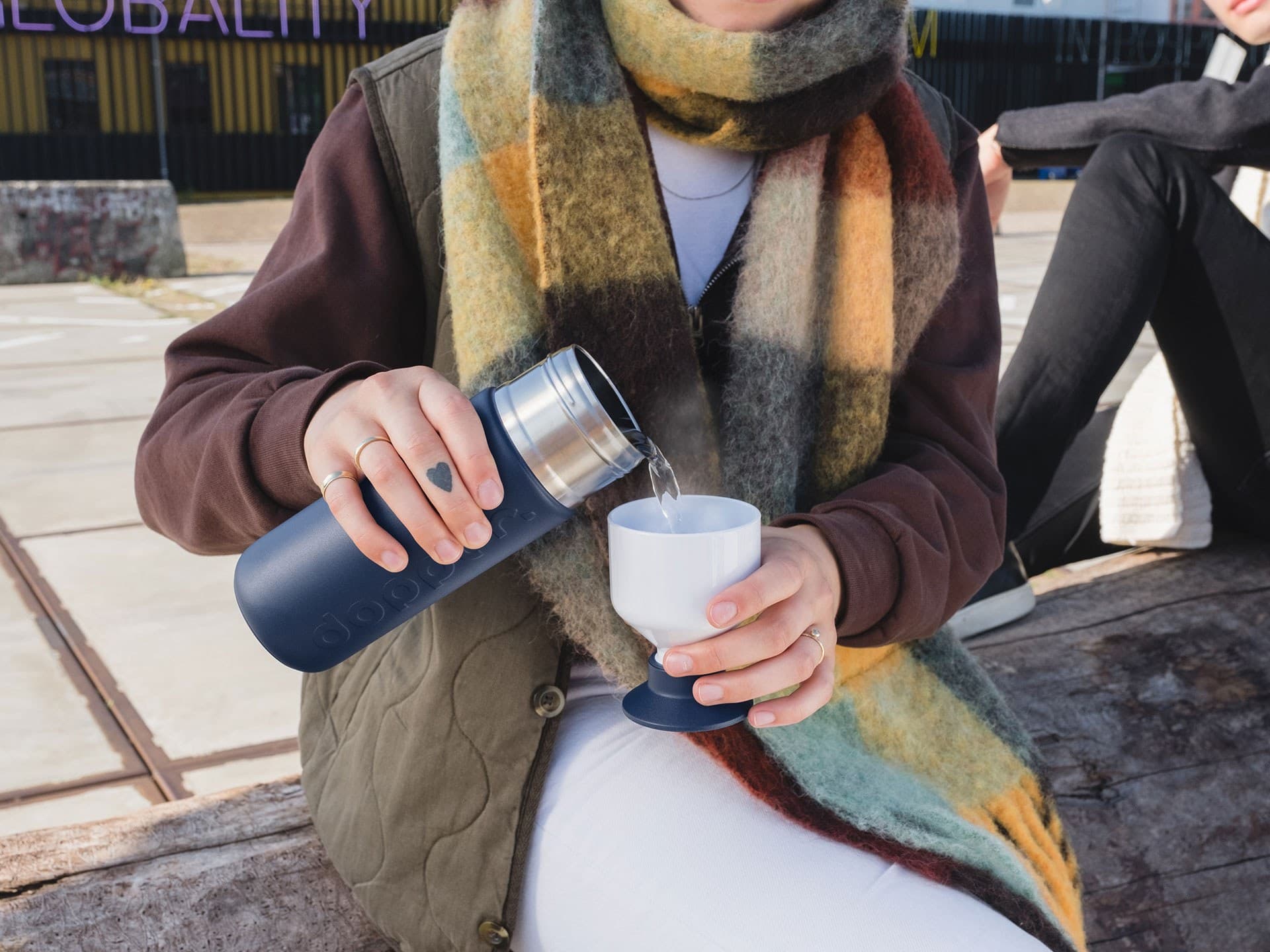 Person pouring water into the cup of a dark blue Dopper Insulated bottle